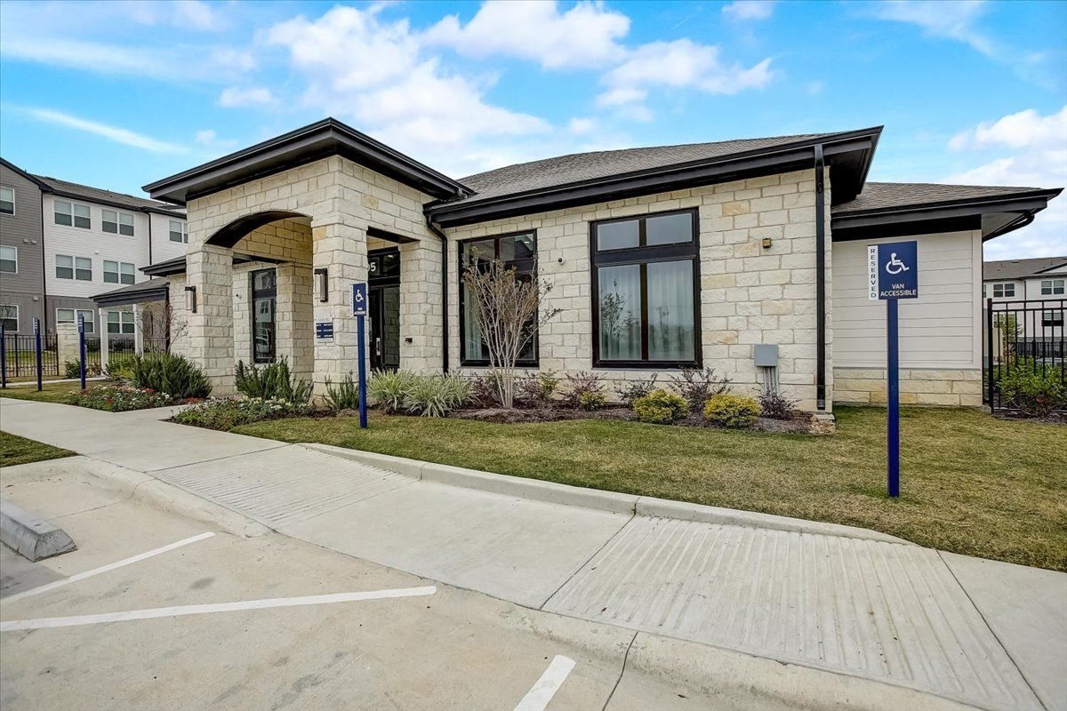 Single-story amenity building with stone façade, large windows, and neatly planted landscaping along the drive.